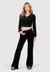 Schwarze Velours-Cropped-Zip-Jacke mit Fronttaschen, kombiniert mit hoch taillierten, weit geschnittenen schwarzen Velours-Hosen mit Kordelzug und Taschen.