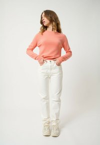 Koraal gebreid sweater, lange mouwen, losse fit, gecombineerd met witte rechte jeans en crèmekleurige sneakers met gestructureerde accenten.