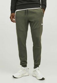 Olijfgroene sweatpants met een tapere pasvorm, gemaakt van een zachte stof. Beschikt over een zijzak, contrasterende panelen en een trekkoord in de taille.