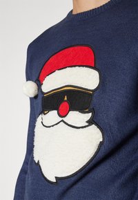 Marineblauer Pullover mit einem Santa-Gesicht-Design, das einen roten Hut und schwarze Sonnenbrillen zeigt, ergänzt durch einen flauschigen weißen Bart und eine rote Nase.