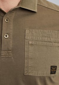 Khaki polo-shirt med struktureret krave, to knappe lukning, forlommes med syning detaljer og et logo-patch på lommen.