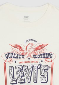 Levi's crèmekleurig t-shirt met een grafische print van een adelaar, sterren en tekst in rood en marineblauw. Ontspannen halslijn. Katoenen materiaal.