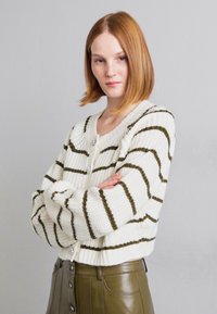 Stripet strikket cardigan i krem med grønne striper, med knappelukking foran og teksturert stoff. Brukt med høyhåndt høyde olivengrønn skjørt.