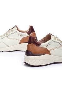 Zapatillas de cuero blancas con acentos en color marrón claro y oscuro, con cordones crema y costuras decorativas, y una suela blanca gruesa para mayor altura.