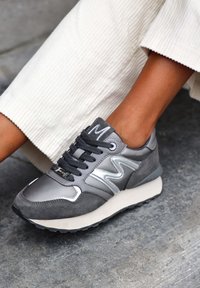Scarpa sportiva grigia con una combinazione di pelle liscia e suede, lacci neri, dettagli argentati e una suola in gomma testurizzata.