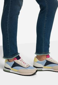 Zapatillas que combinan materiales en azul, rosa, amarillo y beige, con un upper texturizado, cordones blancos y una suela negra.