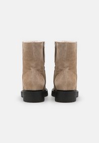 Botas de tobillo de ante beige con suela de goma negra y cremalleras laterales, que cuentan con un suave forro de pelaje y una punta redonda para mayor comodidad.