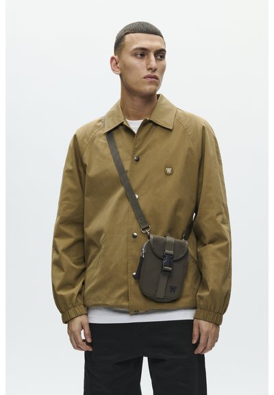 Manteau marron avec col, boutons-pression et poches latérales, accompagné d'un sac bandoulière vert avec rabat et sangle ajustable.