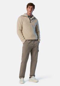 Beiger Rippstrickpullover mit einem halben Reißverschluss-Kragen, kombiniert mit hellbraunen Hosen und weißen Sneakers. Das Outfit hat eine entspannte Passform.