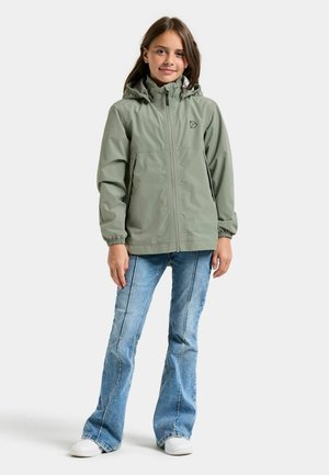 Világoszöld vízálló kapucnis kabát elülső cipzárral és rugalmas mandzsettákkal, világoskék bővülő farmerral és fehér tornacipővel párosítva.