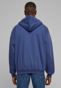 Blå hættetrøje med en afslappet pasform, ribbet kant og manchetter samt glat tekstur. Bagfra ses accentuerede sømme og hætte-design.