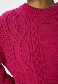 Gebreide magenta trui met diverse texturen, waaronder kabelsteek en ribbelpatronen, met een ronde hals en aansluitende mouwen.