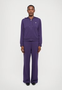 Paarse hoodie en bijpassende sweatpants van zachte stof. De hoodie heeft een rits aan de voorkant en een capuchon met trekkoord. Klassieke pasvorm met lange mouwen.