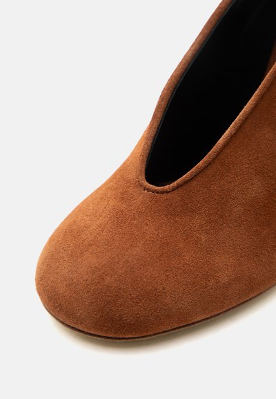 Γυναικείο καφέ σουέντ παπούτσι με στρογγυλερή μύτη και βαθύ V-σχήμα άνοιγμα, απεικονιζόμενο σε κοντινή όψη σε λευκό φόντο.
