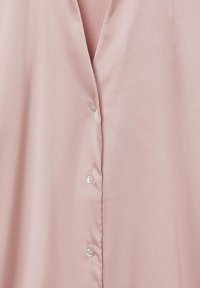 Blusa rosa chiaro realizzata in tessuto morbido, con scollatura a V e bottoni simili a perle disposti davanti. Texture soffice e design semplice.