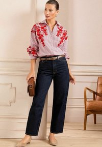 Camicia a righe rossa e bianca con ricami floreali, abbinata a jeans scuri a vita alta e ballerine color tan. Cintura marrone e piccola borsa a tracolla.