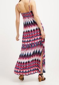 Robe maxi à fines bretelles, présentant un motif en chevrons rose, bleu et blanc. Fente latérale et smocks élastiques au dos.