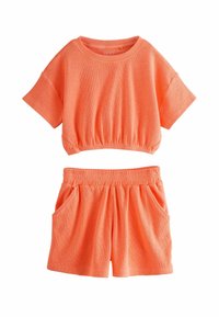 Completo a due pezzi composto da un top corto a maniche corte e da pantaloni corti con vita elastica, entrambi in tessuto a coste arancione e con tasche laterali.