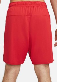 Uomo che indossa pantaloni sportivi rossi semplici, mostrato di spalle, con fascia elastica in vita e peli sulle gambe visibili.