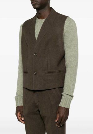 Uomo che indossa un gilet marrone scuro abbottonato sopra un maglione lavorato a maglia grigio chiaro a maniche lunghe con pantaloni marrone scuro coordinati.
