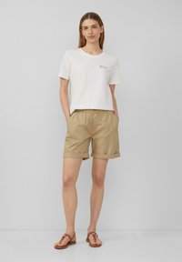 Witte T-shirt met korte mouwen met de tekst "LOVE" in kleurrijke letters; beige, opgerolde shorts van lichtgewicht stof, gecombineerd met bruine sandalen.