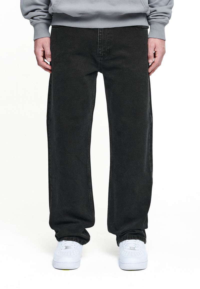 Schwarze Jeans aus Denim mit lockerer Passform, subtilen Nähdetails und geradem Bein, getragen mit weißen Sneakern.