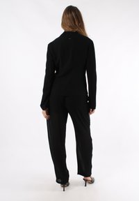 Completo due pezzi nero composto da un top a maniche lunghe e pantaloni larghi. Il tessuto è leggero e leggermente trasparente, con una silhouette pulita.