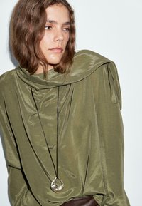 Oliven grøn, draperet langærmet top med tekstureret stof. Har en cowl neck og en asymmetrisk kant. Pendant halskæde inkluderet.