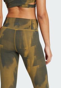 High-waisted leggings in a textured fabric, featuring a green and yellow abstract pattern with a fitted design and subtle branding at the waist.