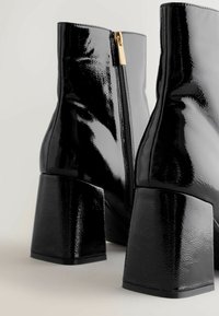 Black patent leather ankle boots with a chunky heel and side zipper detail. Smooth texture with a reflective finish and clean, modern design.
