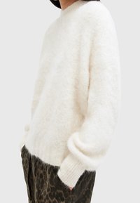 Weißer, flauschiger Strickpullover mit rundem Ausschnitt und überschnittenen Schultern. Rippbündchen an Ärmeln und Saum. Kombiniert mit einer Hose im dunklen Leopardenmuster.