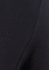 Tissu en maille noire avec une texture lisse, présentant une couture visible. Le matériau semble dense et légèrement élastique, avec un motif subtil.