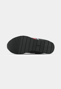 Zwarte sneakersol met gestructureerd rubber, voorzien van horizontale en verticale groeven voor grip. Accentueert met blauwe en rode strepen.