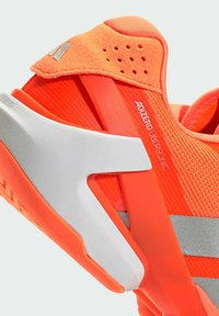 Φωτεινό πορτοκαλί αθλητικό παπούτσι με πλέγμα στην επάνω πλευρά, ασημένιες λεπτομέρειες και υφή στην εξωτερική σόλα. Διαθέτει μαλακό κολάρο και τρύπες για αερισμό.