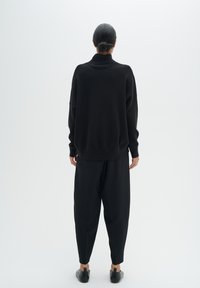 Pulover negru din tricot cu guler înalt, croială lejeră și mâneci lungi, asortat cu pantaloni negri evazați și pantofi negri slip-on.