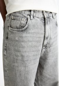Jeans de mezclilla gris con un lavado desgastado, diseño de cinco bolsillos y herrajes metálicos. Presentan un corte recto y una textura de desgastado sutil.