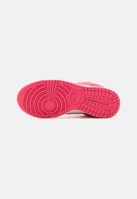 Semelle d'une chaussure Nike rouge montrant des motifs de bande de roulement circulaires et rectangulaires ainsi que le logo Nike au centre.
