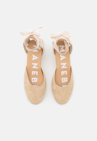 Ballerine beige in suede con tomaia in rete intrecciata e fiocco, dotate di una soletta liscia con la scritta 'MANEBÍ' stampata in lettere bianche in grassetto.