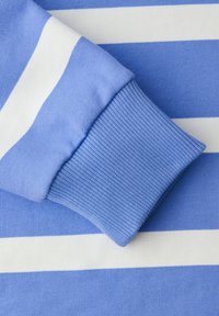 Poignet de chemise à manches longues rayée bleue et blanche avec bandeau tricoté côtelé, sur un fond de tissu rayé assorti.