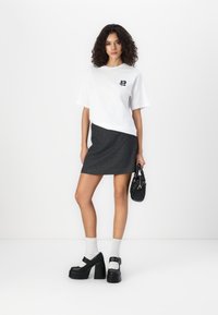 White oversized t-shirt with a black graphic, grey mini skirt, black platform sandals, white socks, and black handbag. Smooth textures.