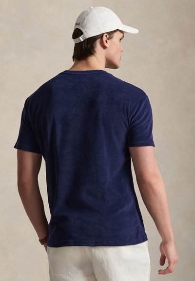 Μπλε σκούρο μπλουζάκι από μαλακό ύφασμα, με στρογγυλή λαιμόκοψη και κοντά μανίκια. Η πίσω όψη δείχνει καθαρές γραμμές και λιτή λεπτομέρεια.