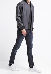 Bomberjakke med grå uldkrop og sorte lærmsleeves, parret med mørke jeans og hvide sneakers. Glat tekstur og tætsiddende design.