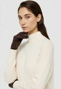 Dunkelbraune Lederhandschuhe, kombiniert mit einem cremefarbenen Rollkragenpullover, der eine glatte Textur und eine figurbetonte Passform betont.