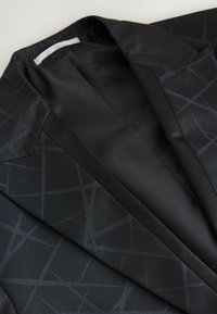 Schwarzer Blazer mit einem subtilen geometrischen Muster, strukturiertem Stoff, scharfem Kragen und glattem Futter. Das Design zeichnet sich durch klare Linien und einen maßgeschneiderten Abschluss aus.