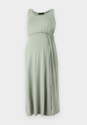 Mouwloze lichtgroene zwangerschapsjurk met tailleband, ronde halslijn en vloeiende midi-lengte rok tegen een witte achtergrond.
