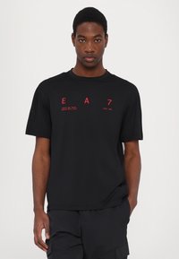 Black short-sleeved t-shirt with red printed text reading "EA 7" and "LIMITS ARE BEING BROKEN WITH STYLE" and "SINCE 2004."
