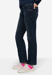 Jeans in denim blu scuro con un design a gamba dritta, caratterizzati da un classico stile a cinque tasche e una sottile texture sbiadita. Indossati con sneakers bianche e rosa.