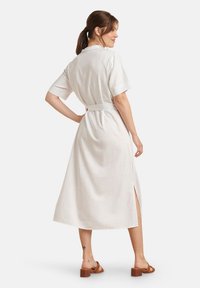 Witte katoenen midi-jurk met korte mouwen, een ceintuurlijn en zijsplitten. Gladde textuur, rechte snit en minimalistisch design.