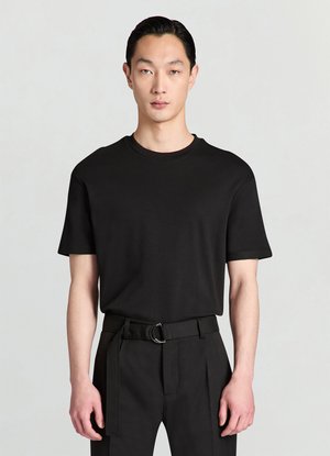 T-shirt nera a maniche corte in tessuto liscio, con scollo rotondo e vestibilità rilassata, abbinata a pantaloni neri sartoriali e cintura.