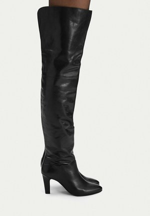 Black knee-high leather boots with pointed toes and mid-height heels worn on legs against plain background.